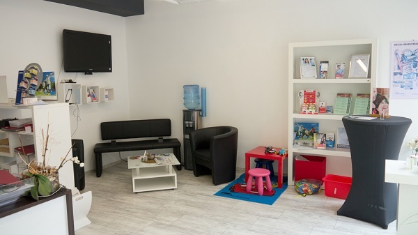 Heller Wartebereich einer Praxis mit Sitzgelegenheiten, Kinderspielecke und Infobroschüren.
